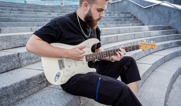 Jeune musicien de rue jouant de la guitare assis sur des marches de granit