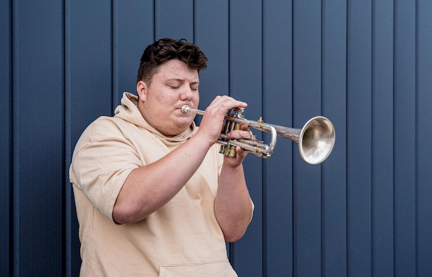 Photo jeune musicien de rue jouant de la trompette près du grand mur bleu