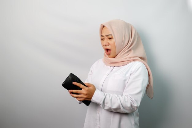 Une jeune musulmane asiatique malheureuse portant un hijab montrant un portefeuille vide isolé sur un fond blanc