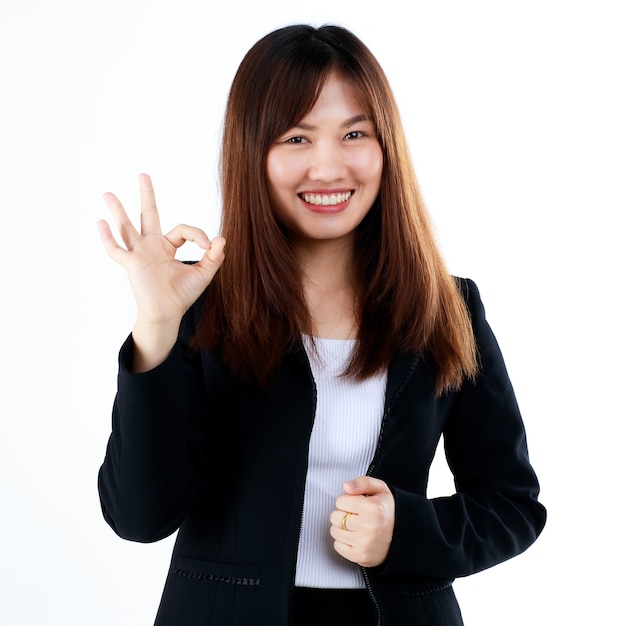 Jeune et nouvelle femme d'affaires asiatique au look gradué en costume pose dans un geste publicitaire, montre les doigts dans le signe OK pour accepter ou approuver quelque chose. Isolé sur fond blanc.