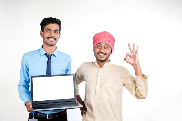 Jeune officier indien montrant un écran d'ordinateur portable avec un agriculteur sur fond blanc.