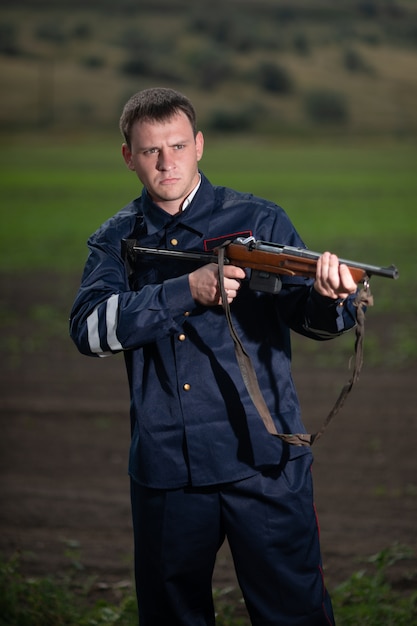 Jeune officier de police en uniforme, avec une arme à la main sur le paysage rural