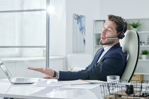 Jeune opérateur de support de service parlant au client à l'aide d'un appareil mains libres dans un bureau moderne