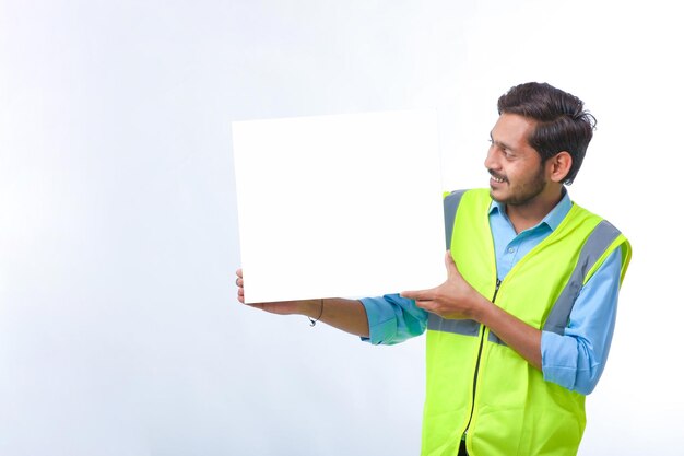 Jeune ouvrier du bâtiment indien montrant un tableau d'affichage vide sur fond blanc.