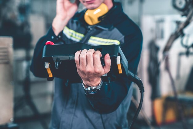 Jeune ouvrier d'usine travaillant avec un bras robotique adepte