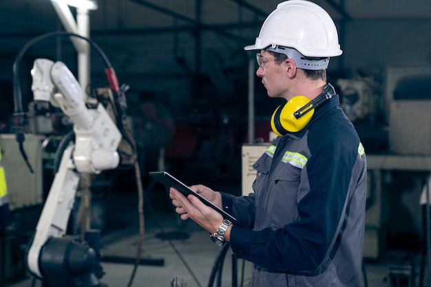 Jeune ouvrier d'usine travaillant avec un bras robotique adepte