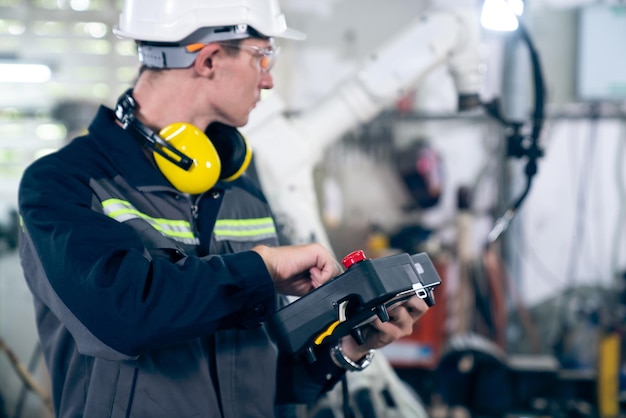 Jeune ouvrier d'usine travaillant avec un bras robotique adepte