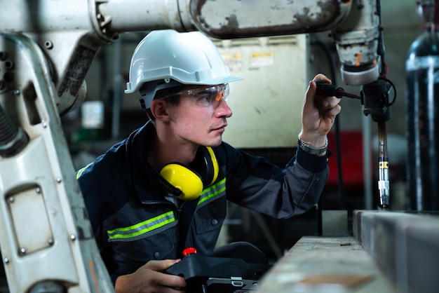 Jeune ouvrier d'usine travaillant avec un bras robotique adepte