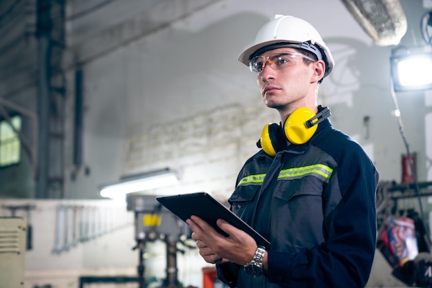 Jeune ouvrier d'usine utilisant un ordinateur tablette adepte dans un bâtiment d'atelier