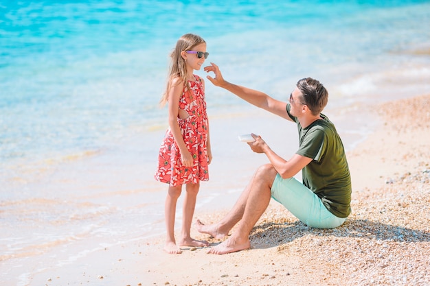 Jeune papa appliquant une crème solaire au nez de sa fille sur la plage. protection solaire