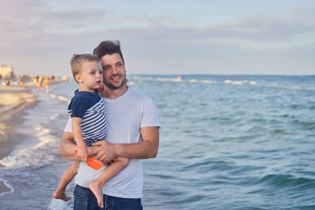 Jeune papa du Caucase avec petit-fils marche une chaude journée d'été le long de la côte de la mer. Concept de vacances en famille d'été. Père et fils d'amitié.