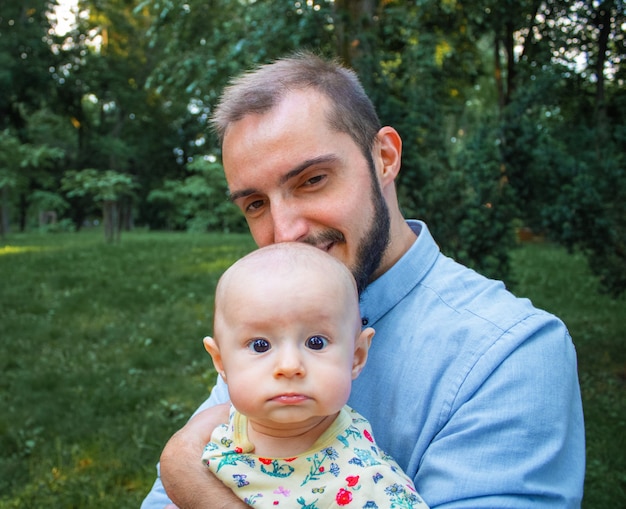 Jeune papa tenant son bébé sur le fond d'un paysage d'été. Le père est heureux et souriant, le nouveau-né avec une expression de visage confuse.