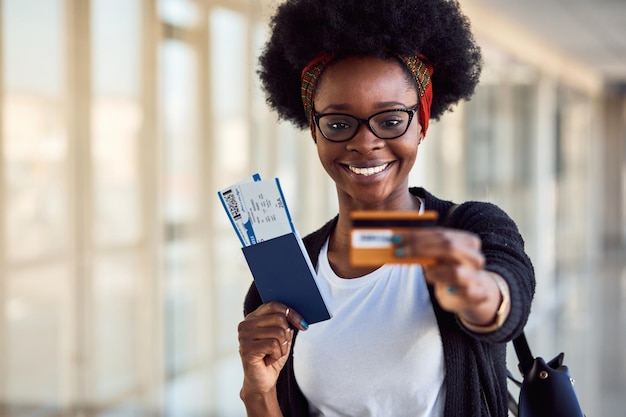 Une jeune passagère afro-américaine en vêtements décontractés est à l'aéroport avec des billets et une carte de crédit.