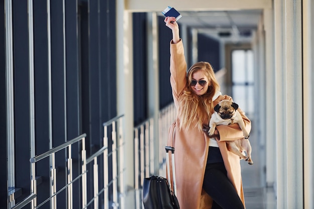 Jeune passagère en vêtements chauds marchant avec son chien dans le hall de l'aéroport.