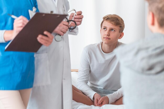 Un jeune patient adolescent est assis en tailleur sur un lit d'hôpital pendant son hospitalisation