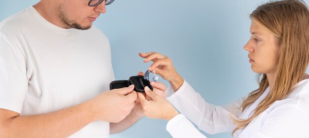 jeune patient masculin testant une aide auditive dans la salle d'examen de la clinique médecin aidant
