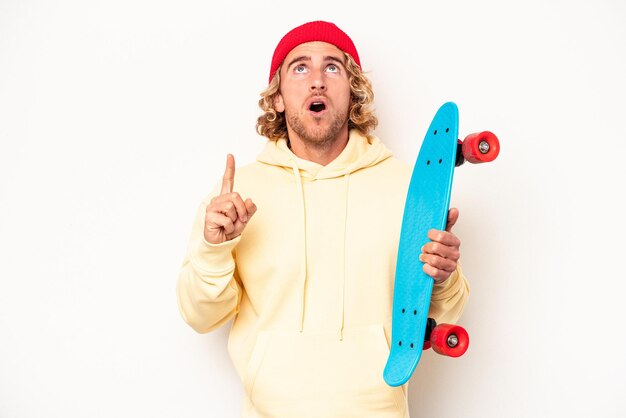 Jeune patineur caucasien isolé sur fond blanc pointant vers le haut avec la bouche ouverte.