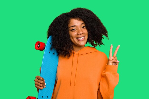 Photo jeune patineuse femme afro-américaine tenant un petit patin isolé montrant le numéro deux avec les doigts