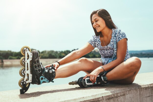 Une jeune patineuse s'amuse sur la rive de la rivière de la ville et attache ses rouleaux par une belle journée d'été.