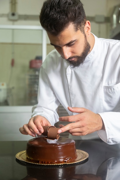 Jeune pâtissier finissant la décoration d'un gâteau au chocolat