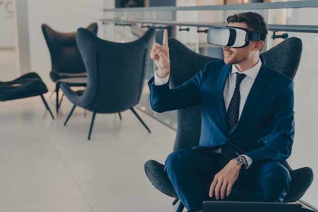 Jeune PDG assis dans le hall du centre de bureaux avec des lunettes de casque vr pointant avec l'index en l'air