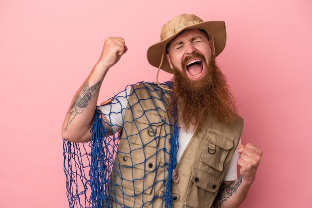 Jeune pêcheur de gingembre caucasien avec longue barbe tenant un filet isolé sur fond rose