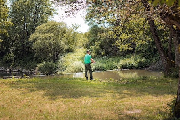 Un jeune pêcheur pêche sur la rive d'une rivière entourée d'une belle nature verte en utilisant de petits poissons comme