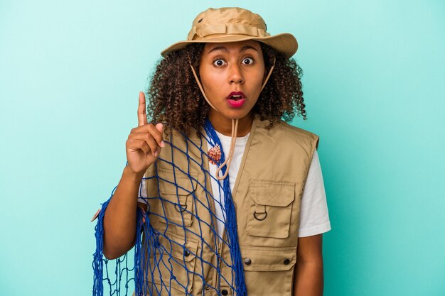 Jeune pêcheuse afro-américaine tenant un filet isolé sur fond bleu ayant une idée, un concept d'inspiration.