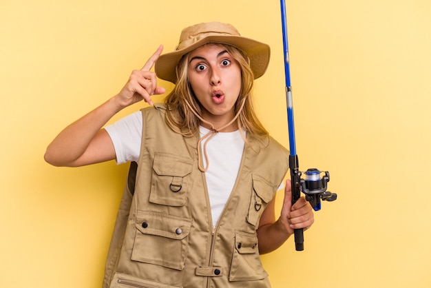 Jeune pêcheuse blonde caucasienne tenant une tige isolée sur fond jaune ayant une idée, un concept d'inspiration.