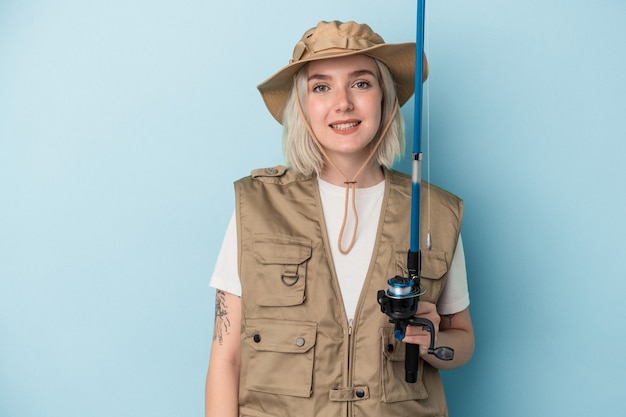 Jeune pêcheuse caucasienne tenant une tige isolée sur fond bleu heureuse, souriante et joyeuse.