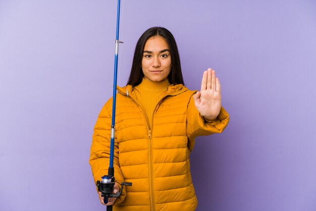 Jeune pêcheuse isolée sur un mur violet debout avec la main tendue montrant le panneau d'arrêt, vous empêchant.