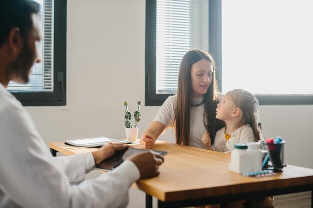 Photo un jeune pédiatre avec une tablette à la main consulte une mère avec sa petite fille.