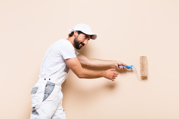 Jeune peintre barbu peignant un mur avec un rouleau à peinture