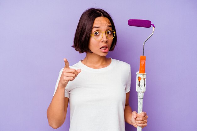 Jeune peintre métisse femme tenant un bâton de peinture isolé sur fond violet ayant une idée, un concept d'inspiration.