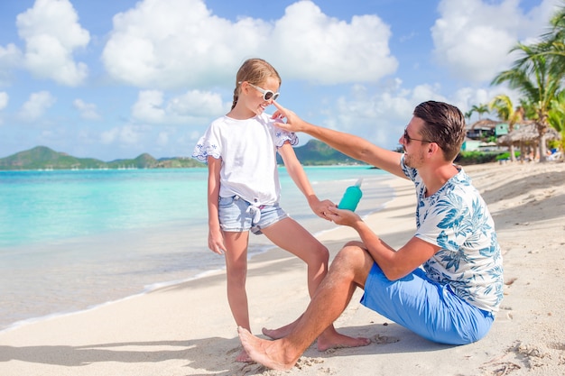 Jeune père, appliquer la crème solaire au nez de la fille sur la plage. protection solaire