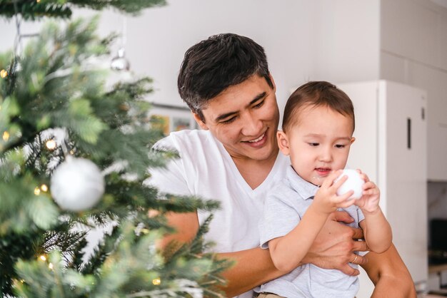 Photo un jeune père asiatique et son adorable petit fils décorent ensemble l'arbre de noël à la maison.