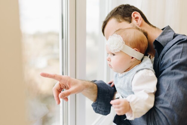 Jeune père caucasien montrant sa petite fille quelque chose dans la fenêtre