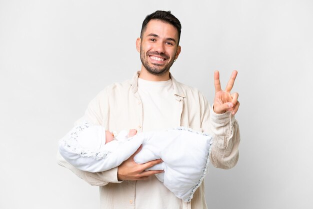 Jeune père caucasien avec son bébé nouveau-né sur fond isolé souriant et montrant le signe de la victoire