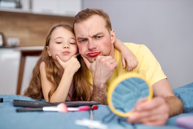 Jeune père et enfant fille regarde la réflexion sur le petit miroir ayant le maquillage du visage