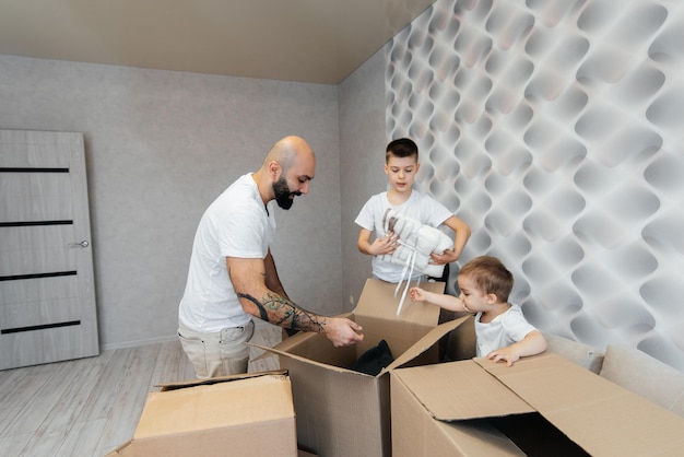 Un jeune père avec des enfants déballe une boîte de choses après avoir déménagé dans un nouvel appartement Achat de biens immobiliers Livraison de pendaison de crémaillère et transport de marchandises