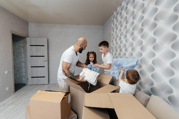 Un jeune père avec des enfants déballe une boîte de choses après avoir déménagé dans un nouvel appartement Achat de biens immobiliers Livraison de pendaison de crémaillère et transport de marchandises