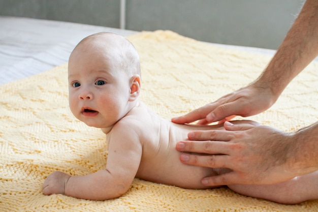 Jeune père fait massage pour bébé bébé heureux sur un plaid tricoté jaune