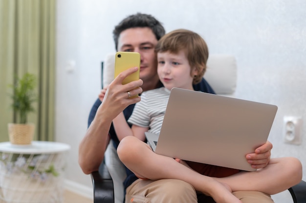 Jeune père avec fils à l'aide d'un ordinateur portable et d'un smartphone.