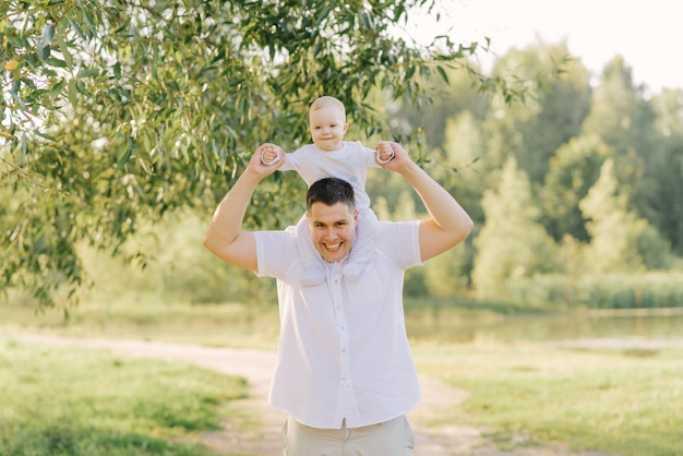 Un jeune père heureux de grande taille tient son petit fils autour de son cou dans le parc en été