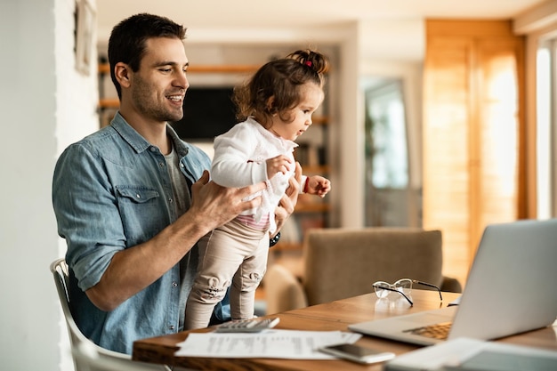 Jeune père heureux s'amusant avec sa petite fille tout en travaillant à la maison