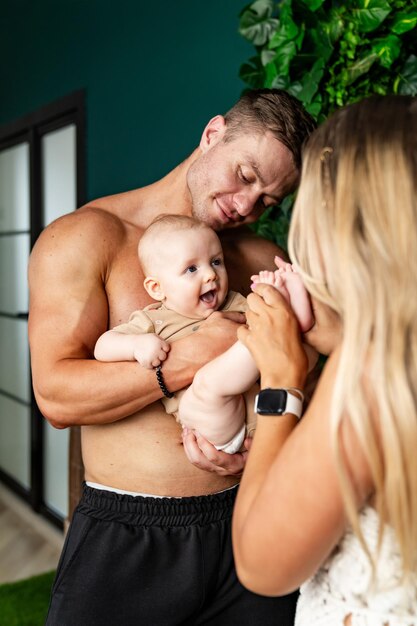 Un jeune père et une jeune mère tiennent leur bébé dans leurs bras et se sourient.