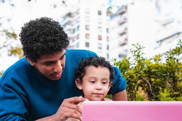 Jeune père noir avec son fils lors d'un appel vidéo avec un ordinateur rose à l'extérieur du concept de fête des pères