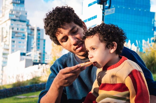 Jeune père à la peau noire avec son fils dans un carré mangeant un concept de style de vie de pizza