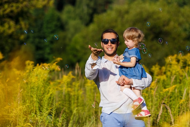 Jeune père avec sa petite fille essayant d'attraper des bulles de savon