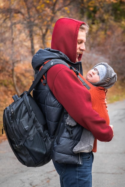 Jeune père avec son bébé dans un porte-bébé ergonomique en randonnée d'automne